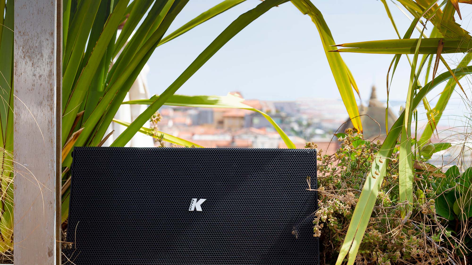 Close-up product image of a K Array speaker in someone's yard